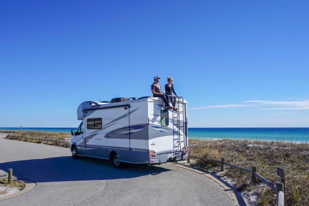 Young couple sitting on the roof of a motorhome overlooking the ocean