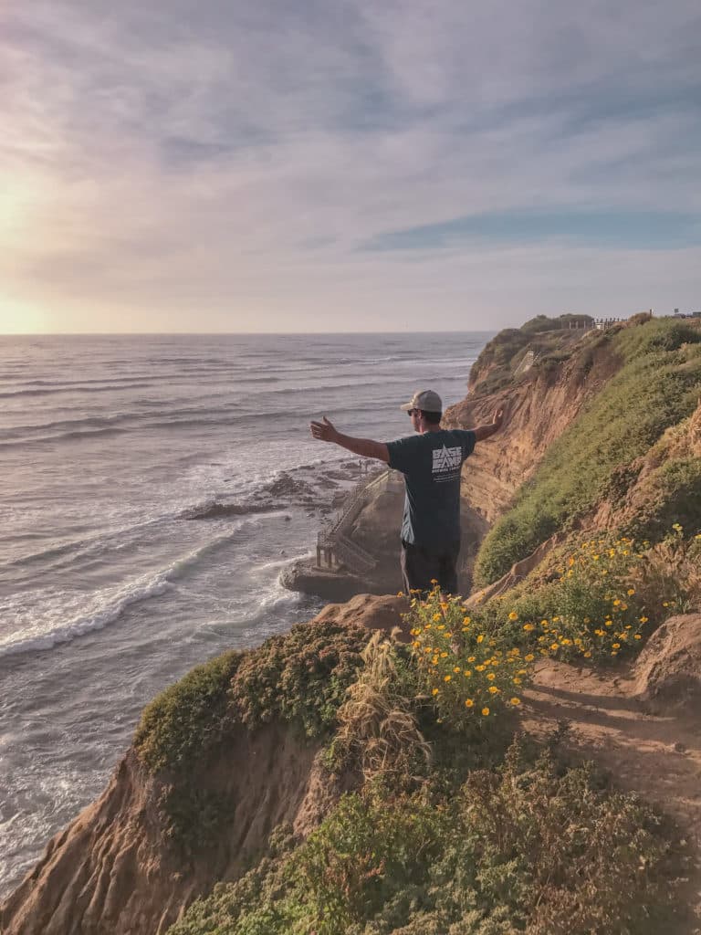 Man on edge of cliff overlooking the ocean with arms up