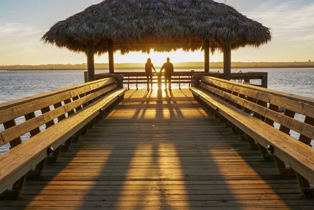 Couple standing at the end of a pier watching the sunset and holding hands in St. Augustine Florida