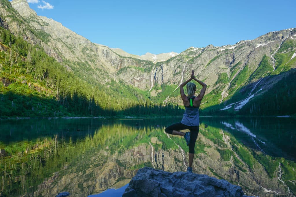 woman doing tree pose yoga in front of a reflective lake in glacier national park