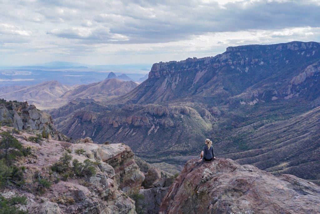 Woman sitting on the edge of a cliff overlooking stunning mountain views in Big Bend National park Texas