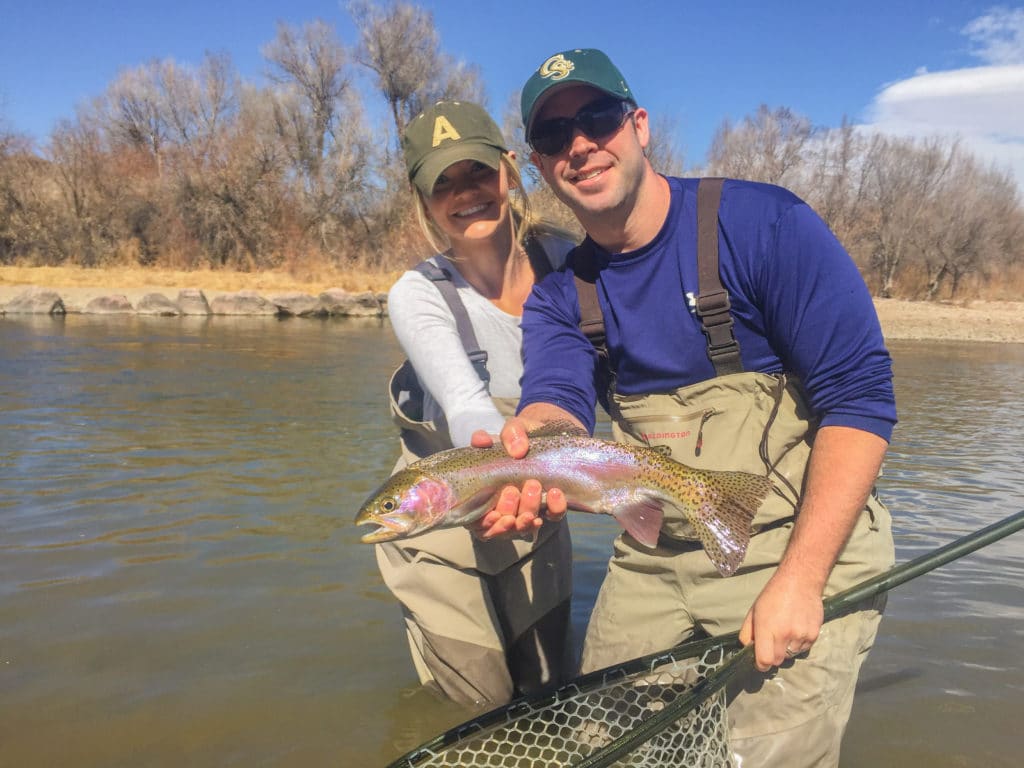 Couple fly fishing holding up a rainbow trout in Colorado