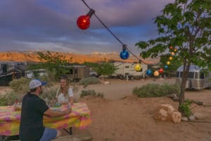 couple camping eating at picnic table with string lights