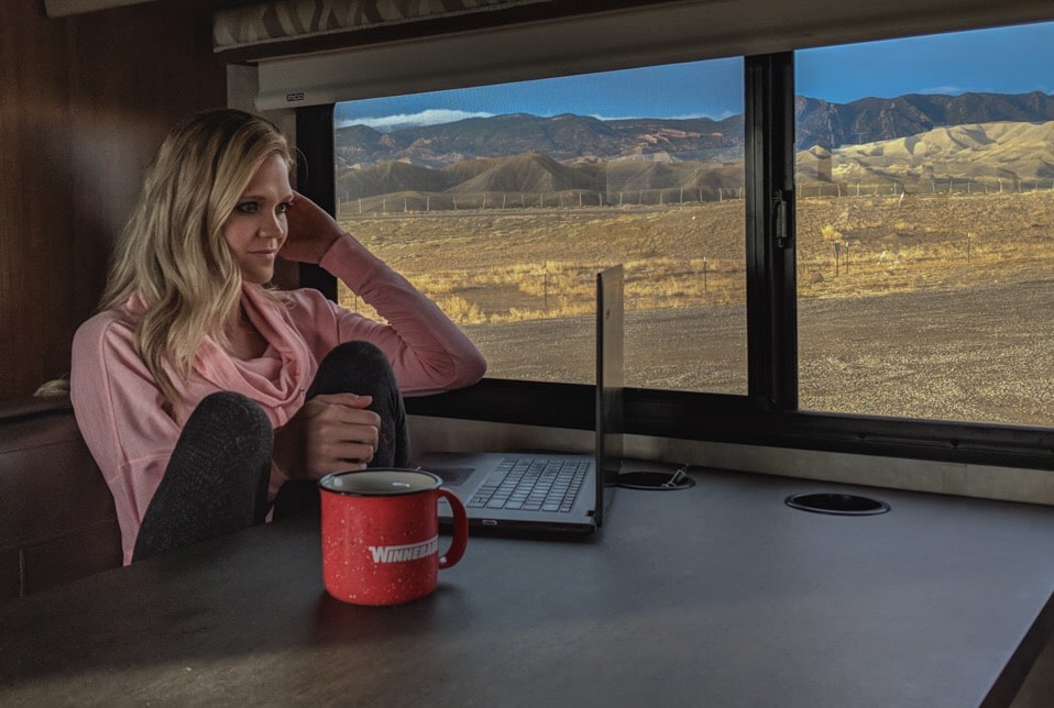 woman working on laptop in RV with mountain views outside window