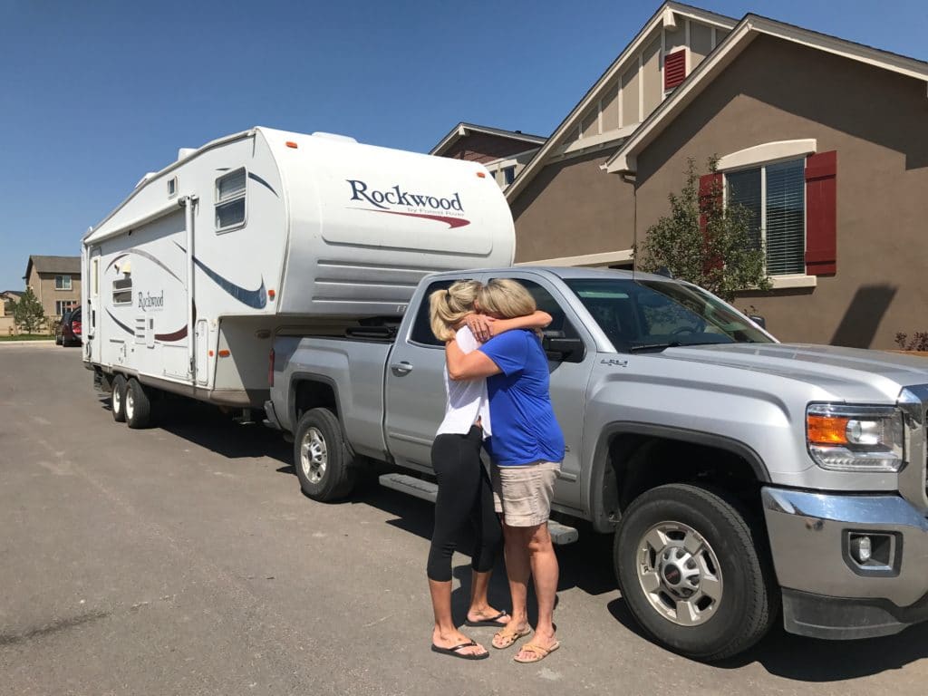 young woman hugging her mom goodbye next to her RV and truck