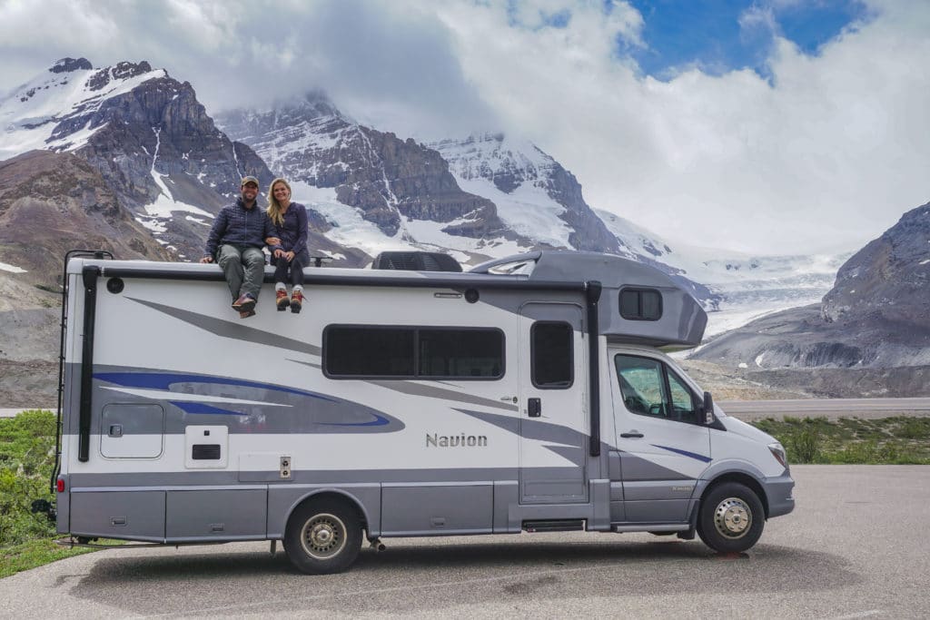 couple sitting on the roof of RV in front of glacier in jasper national park canada