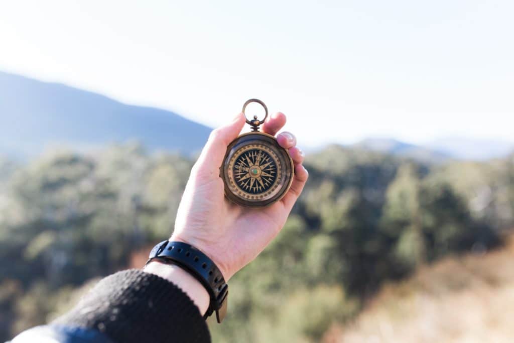 hand stretched out holding a compass with mountain trail in background