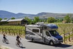 Couple riding bikes next to motohome parked at a vineyard using Harvest Hosts membership