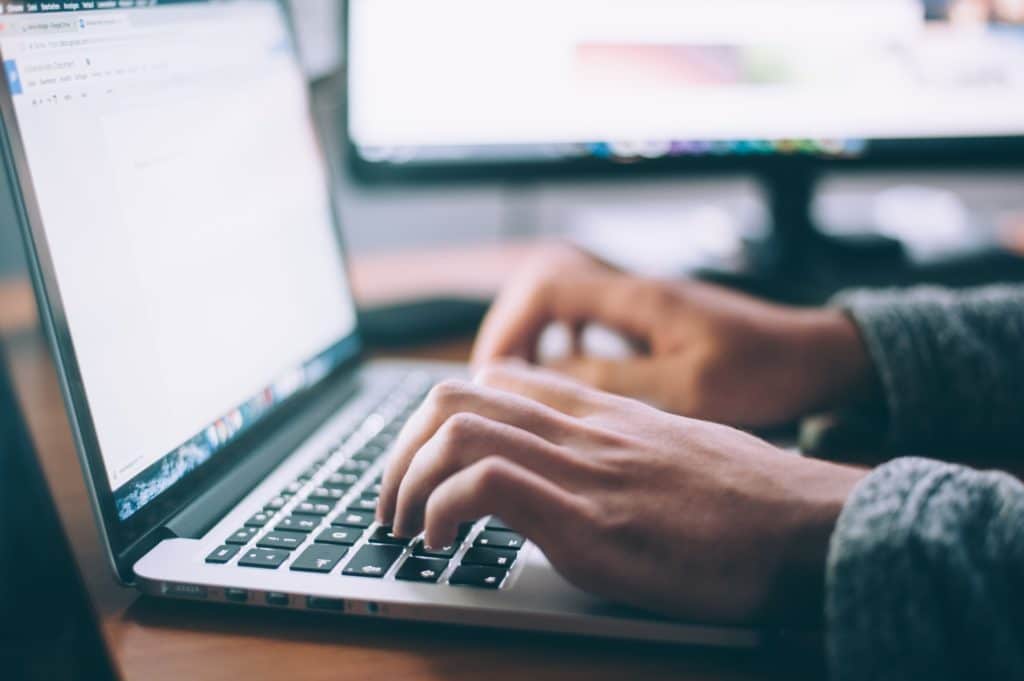 a womans hands typing on a laptop