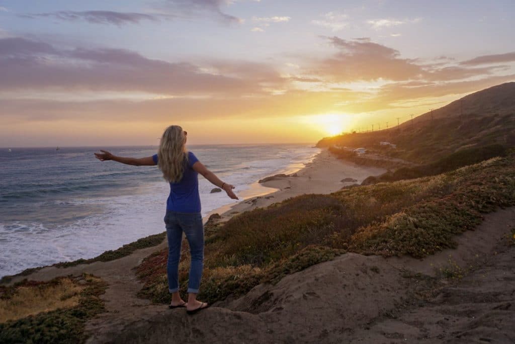 Woman with open arms towards sunset on a California beach