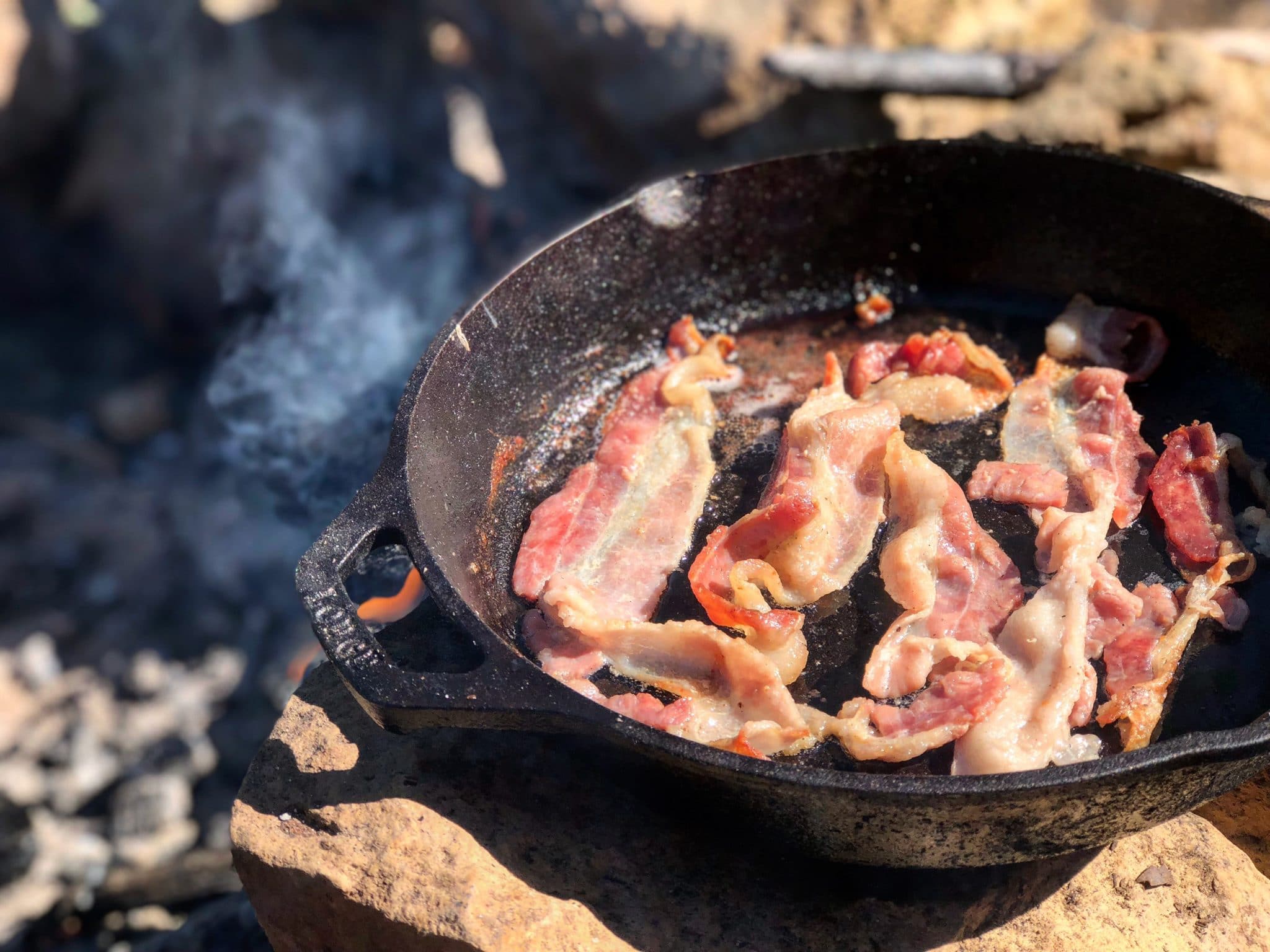 Bacon cooking on a pan over a campfire