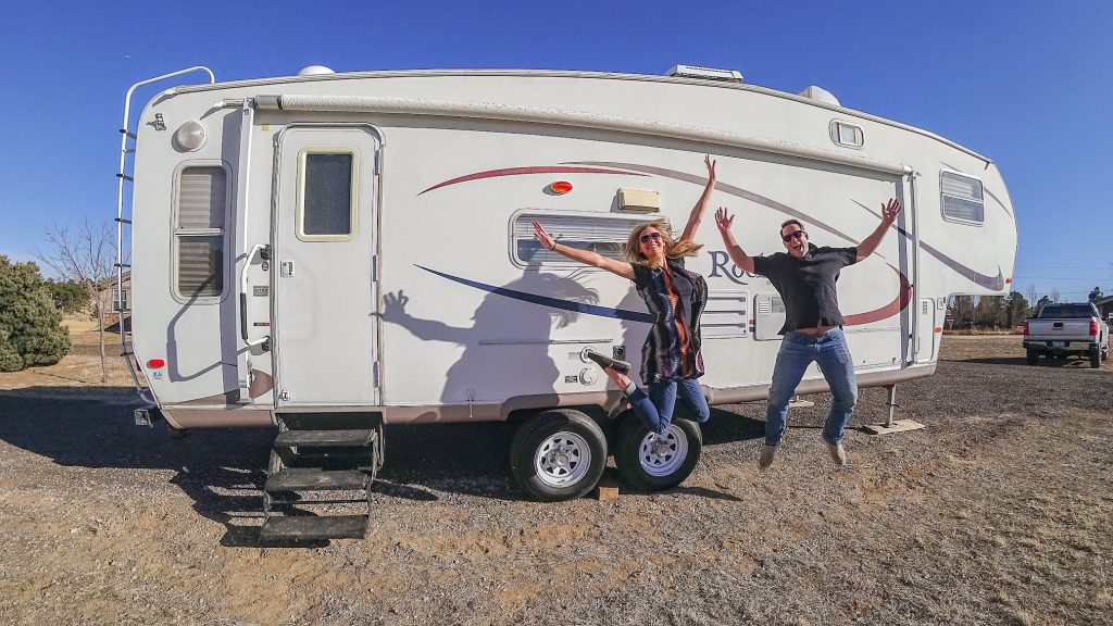 Couple jumping in the air in front of a fifth wheel RV