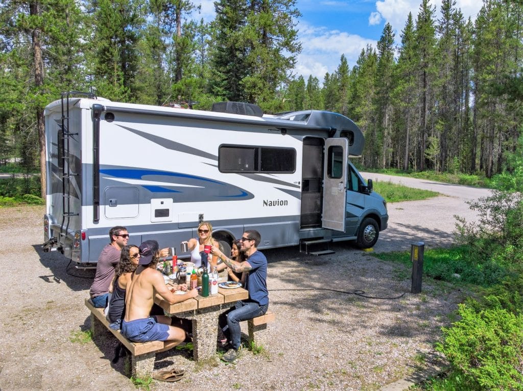 Young friends cheersing and having a meal outside of an RV in a campground in Canada