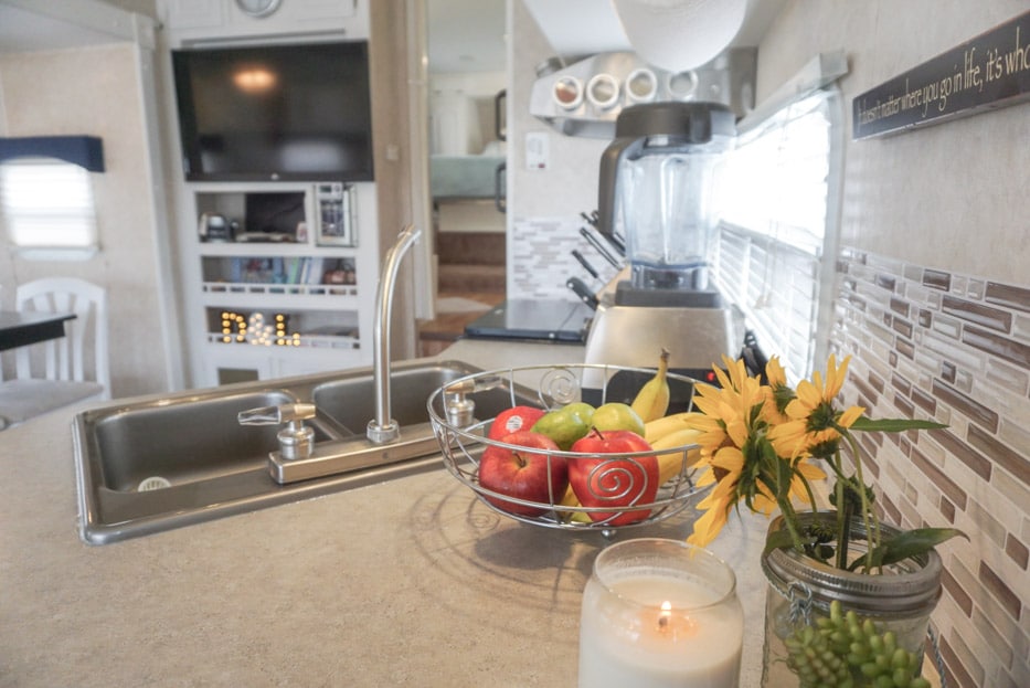 An RV kitchen counter with flowers a fruit bowl and a blender