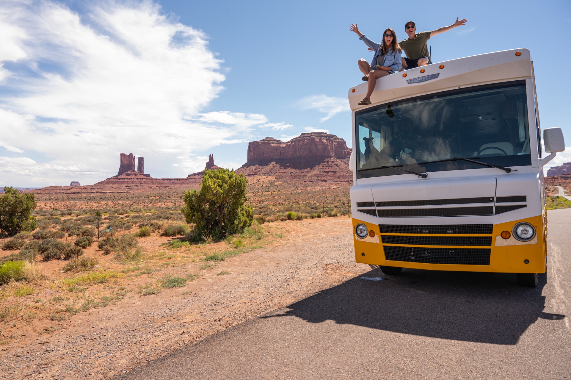 Couple sitting on roof of RV with arms stretched out in the desert