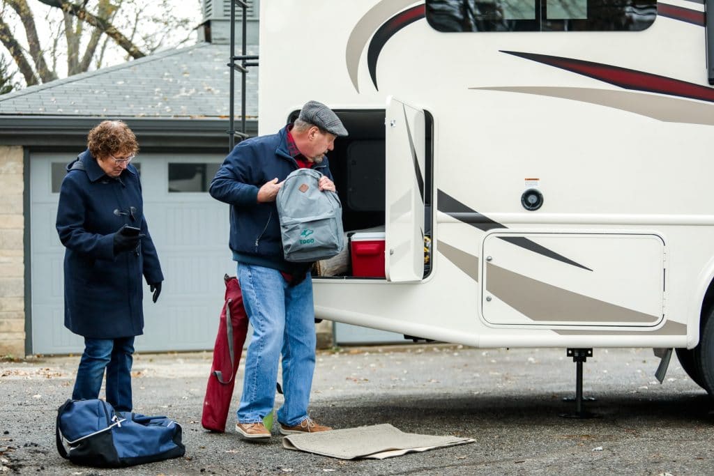 Older couple putting items in exterior storage compartment of motorhome RV