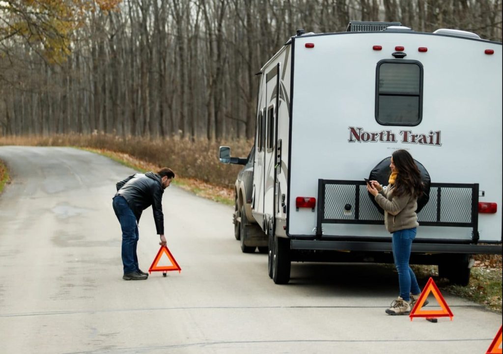 Couple with orange signals pulled over on the side of the road with an RV travel trailer