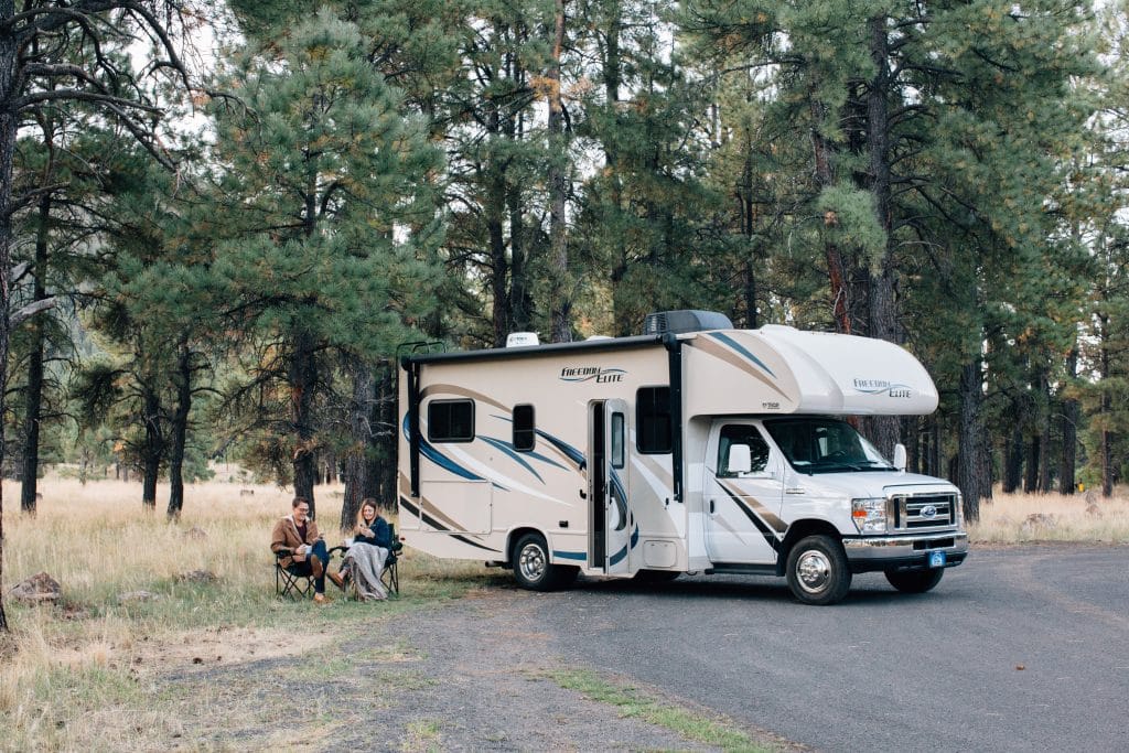 couple sitting outside of motorhome in the woods